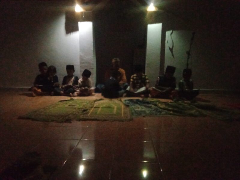 Anak-anak mengikuti pembelajaran mengaji di Musholla An-Nuur dengan penerangan terbatas akibat gangguan listrik.