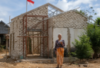 Ibu Fatiha berdiri di depan rumahnya di Desa Ambunten Barat, Sumenep, yang masih dalam proses renovasi. Rumah tersebut sebelumnya berada dalam kondisi memprihatinkan dan nyaris roboh sebelum mendapat bantuan renovasi melalui inisiatif BAZNAS Sumenep. Di atas bangunan itu, bendera Merah Putih tetap berkibar sebagai simbol kecintaan Fatiha terhadap Tanah Air.
